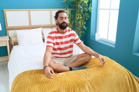 Photo pour Young hispanic man doing yoga exercise sitting on bed at bedroom - image libre de droit