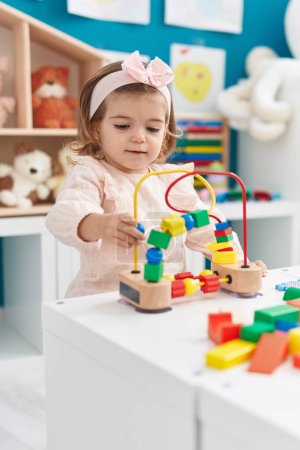 Téléchargez les photos : Adorable bambin blonde jouant avec des jouets debout à la maternelle - en image libre de droit