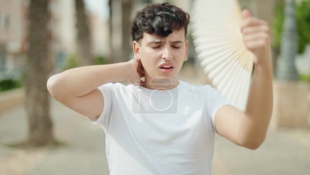 Photo for Non binary man using handfan suffering for hot at park - Royalty Free Image