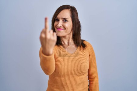 Foto de Middle age brunette woman standing wearing orange sweater showing middle finger, impolite and rude fuck off expression - Imagen libre de derechos