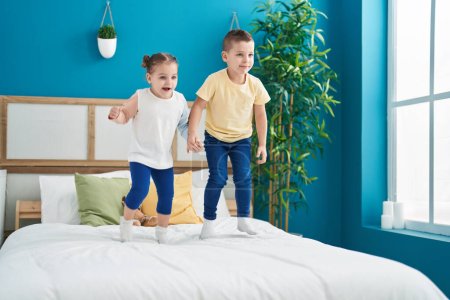 Téléchargez les photos : Deux enfants souriants confiants sautant sur le lit dans la chambre - en image libre de droit