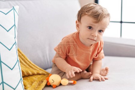 Photo for Adorable blond toddler sitting on sofa at home - Royalty Free Image
