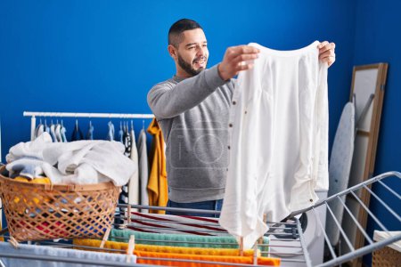 Photo for Young latin man smiling confident hanging clothes on clothesline at laundry room - Royalty Free Image