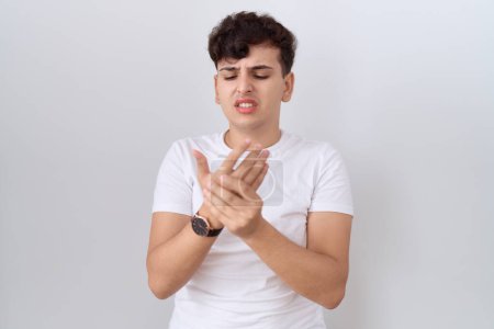 Foto de Hombre joven no binario con camiseta blanca casual que sufre dolor en las manos y los dedos, inflamación de la artritis - Imagen libre de derechos