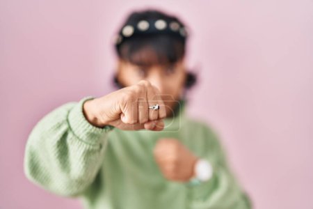 Téléchargez les photos : Young beautiful woman standing over pink background punching fist to fight, aggressive and angry attack, threat and violence - en image libre de droit