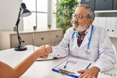 Téléchargez les photos : Homme âgé aux cheveux gris médecin et patient se serrent la main à la clinique - en image libre de droit