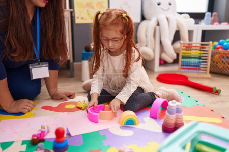 Photo pour Adorable redhead girl playing with toys sitting on floor at kindergarten - image libre de droit