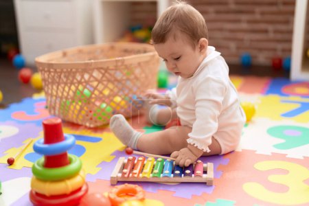 Photo for Adorable toddler touching xylophone sitting on floor at kindergarten - Royalty Free Image