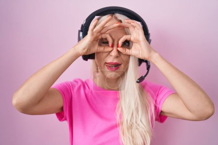 Photo for Caucasian woman listening to music using headphones doing ok gesture like binoculars sticking tongue out, eyes looking through fingers. crazy expression. - Royalty Free Image