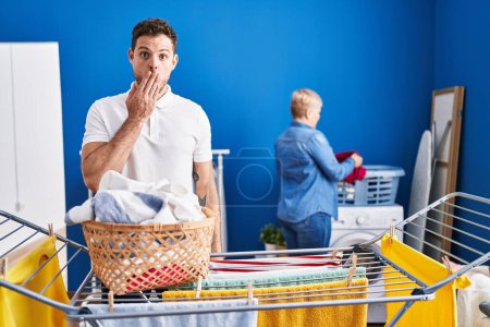 Photo for Hispanic mother and son hanging clothes at clothesline covering mouth with hand, shocked and afraid for mistake. surprised expression - Royalty Free Image