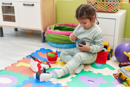 Photo for Adorable hispanic toddler playing with supermarket toy sitting on floor at kindergarten - Royalty Free Image