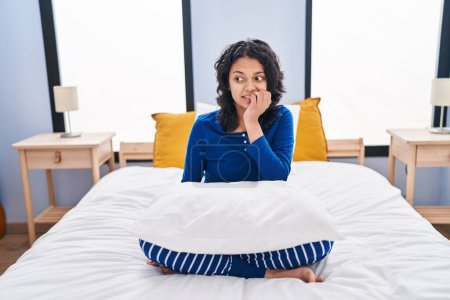 Photo for Hispanic woman with dark hair sitting on the bed at home looking stressed and nervous with hands on mouth biting nails. anxiety problem. - Royalty Free Image