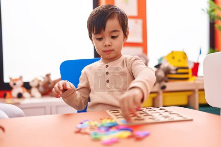Téléchargez les photos : Adorable garçon hispanique jouer avec des mathématiques jeu de puzzle assis sur la table à la maternelle - en image libre de droit
