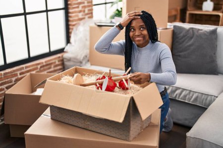 Foto de Mujer afroamericana mudándose a una nueva casa abriendo cajas estresadas y frustradas con la mano en la cabeza, cara sorprendida y enojada - Imagen libre de derechos