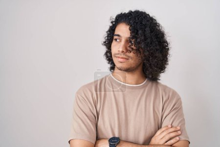 Téléchargez les photos : Hispanic man with curly hair standing over white background looking to the side with arms crossed convinced and confident - en image libre de droit