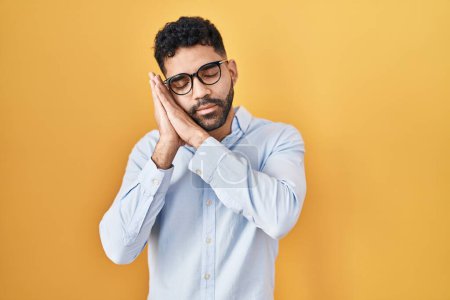 Photo for Hispanic man with beard standing over yellow background sleeping tired dreaming and posing with hands together while smiling with closed eyes. - Royalty Free Image