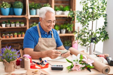 Téléchargez les photos : Middle age grey-haired man florist smiling confident counting dollars at florist - en image libre de droit
