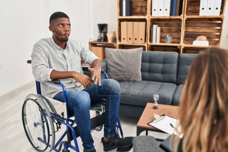 Foto de African american man doing therapy sitting on wheelchair making fish face with lips, crazy and comical gesture. funny expression. - Imagen libre de derechos