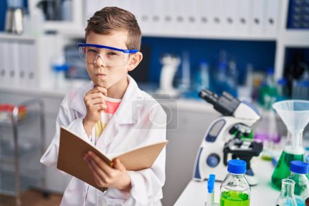 Foto de Blond child wearing scientist uniform reading book at laboratory - Imagen libre de derechos