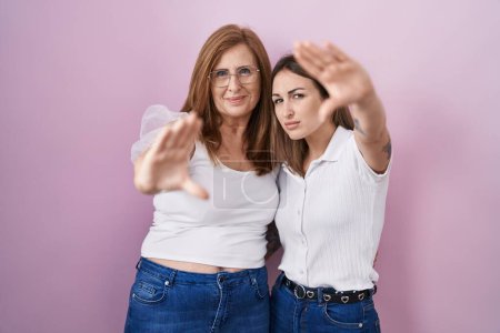 Téléchargez les photos : Hispanic mother and daughter wearing casual white t shirt over pink background doing frame using hands palms and fingers, camera perspective - en image libre de droit