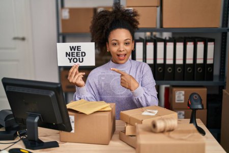 Téléchargez les photos : Jeune femme afro-américaine travaillant dans une petite entreprise e-commerce tenant bannière souriant heureux pointant avec la main et le doigt - en image libre de droit