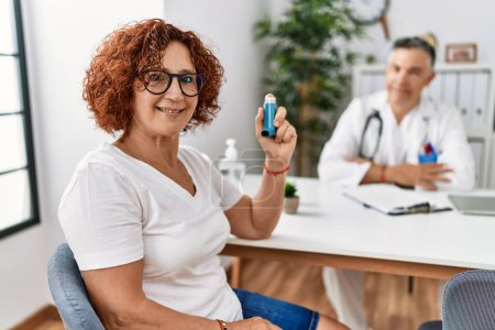 Photo for Middle age man and woman wearing doctor uniform having medical consultation holding inhaler at clinic - Royalty Free Image