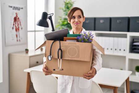 Photo for Middle age doctor woman holding cardboard box with items at the clinic smiling looking to the side and staring away thinking. - Royalty Free Image