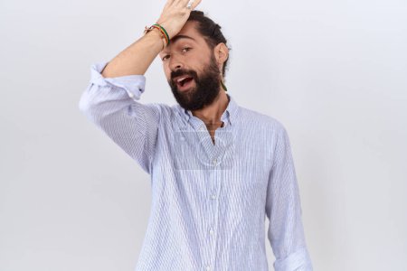 Foto de Hombre hispano con barba vistiendo camisa casual sorprendido con la mano en la cabeza por error, recordar el error. olvidado, mal concepto de memoria. - Imagen libre de derechos