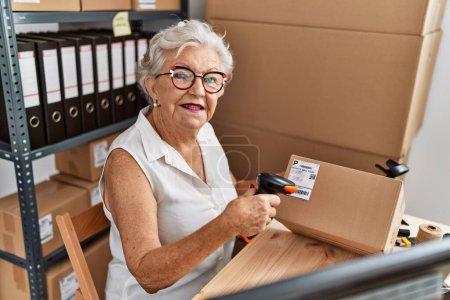 Foto de Senior mujer de pelo gris trabajador de negocios escaneo etiqueta del paquete en la oficina - Imagen libre de derechos