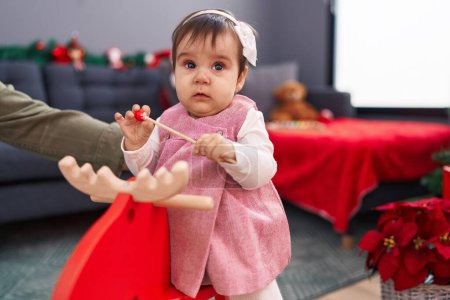 Photo for Adorable hispanic baby playing with reindeer rocking by christmas decoration at home - Royalty Free Image
