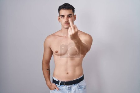 Handsome hispanic man standing shirtless showing middle finger, impolite and rude fuck off expression 