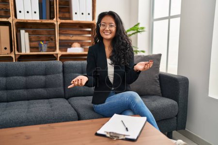 Foto de Joven mujer asiática en consulta oficina sonriente alegre con los brazos abiertos como bienvenida amistosa, saludos positivos y seguros - Imagen libre de derechos