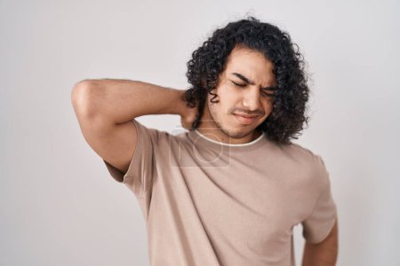 Téléchargez les photos : Homme hispanique avec les cheveux bouclés debout sur fond blanc souffrant de douleur au cou blessure, toucher le cou avec la main, douleur musculaire - en image libre de droit