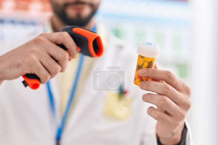 Foto de Hombre árabe joven farmacéutico escaneo píldoras botella en la farmacia - Imagen libre de derechos