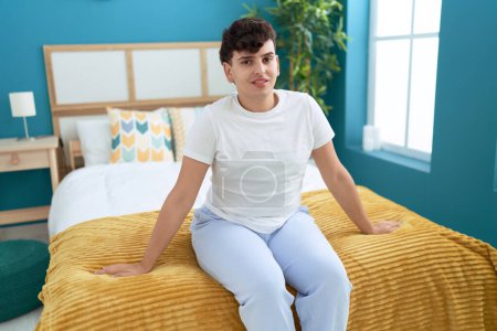 Téléchargez les photos : Non binary man smiling confident sitting on bed at bedroom - en image libre de droit