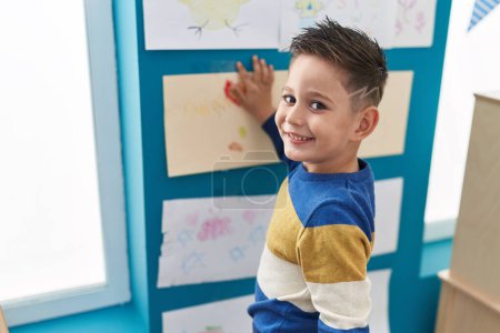 Téléchargez les photos : Adorable garçon hispanique préscolaire étudiant accroché au mur à la salle de classe - en image libre de droit