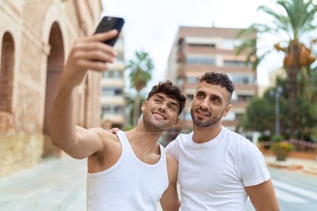 Foto de Dos hombres hispanos pareja sonriendo confiado hacer selfie por teléfono inteligente en la calle - Imagen libre de derechos