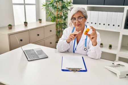 Téléchargez les photos : Femme d'âge moyen portant un uniforme de médecin prescrire des pilules traitement à la clinique - en image libre de droit