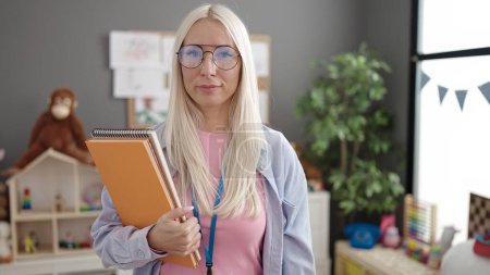 Téléchargez les photos : Young blonde woman preschool teacher holding books at kindergarten - en image libre de droit