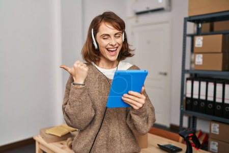 Foto de Young beautiful woman working at small business ecommerce pointing thumb up to the side smiling happy with open mouth - Imagen libre de derechos