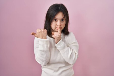 Téléchargez les photos : Woman with down syndrome standing over pink background asking to be quiet with finger on lips pointing with hand to the side. silence and secret concept. - en image libre de droit