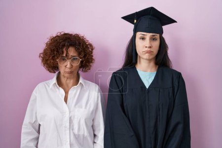 Foto de Hispanic mother and daughter wearing graduation cap and ceremony robe depressed and worry for distress, crying angry and afraid. sad expression. - Imagen libre de derechos