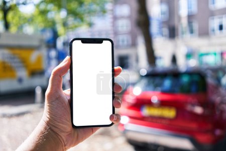Téléchargez les photos : Homme tenant smartphone montrant écran blanc vierge au parking - en image libre de droit