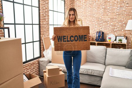 Photo for Young blonde woman holding welcome doormat at new home skeptic and nervous, frowning upset because of problem. negative person. - Royalty Free Image
