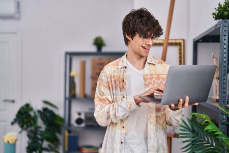 Téléchargez les photos : Young hispanic man artist smiling confident using laptop at art studio - en image libre de droit