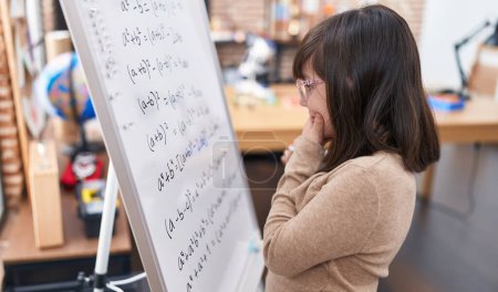 Téléchargez les photos : Adorable hispanique fille étudiante debout par tableau à la résolution des mathématiques exercice en classe - en image libre de droit