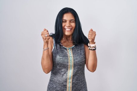 Téléchargez les photos : Mature hispanic woman standing over white background excited for success with arms raised and eyes closed celebrating victory smiling. winner concept. - en image libre de droit
