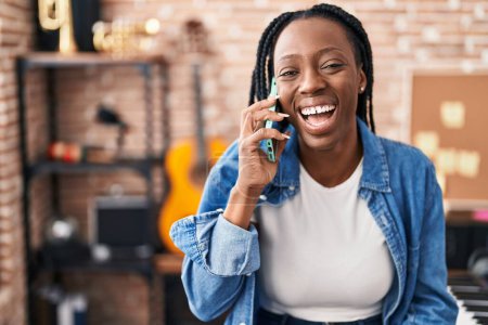 Foto de Artista afroamericana sonriendo confiada hablando en smartphone en estudio de música - Imagen libre de derechos