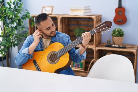 Foto de Joven hispano tocando la guitarra clásica sentado en la mesa en casa - Imagen libre de derechos
