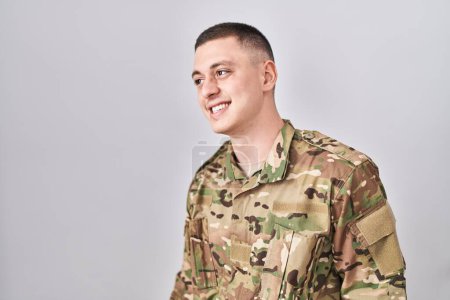 Téléchargez les photos : Young man wearing camouflage army uniform looking away to side with smile on face, natural expression. laughing confident. - en image libre de droit